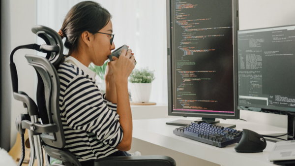 Lo sviluppatore beve caffè durante la revisione del codice su doppio monitor.